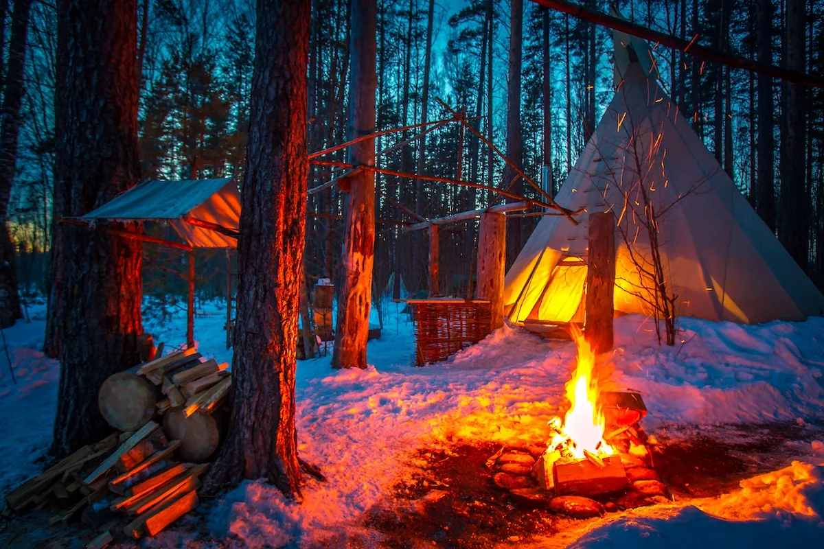 En opplyst lavvo og bål i snødekket skog; midlertidig bilde fra Rjukan Adventure